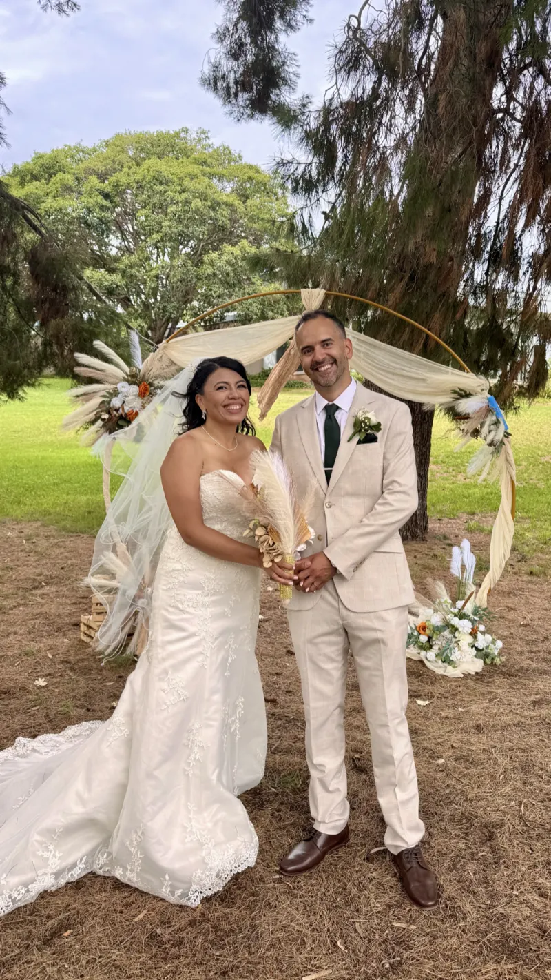 A newly married couple smiling in front of a floral arch at their outdoor garden ceremony